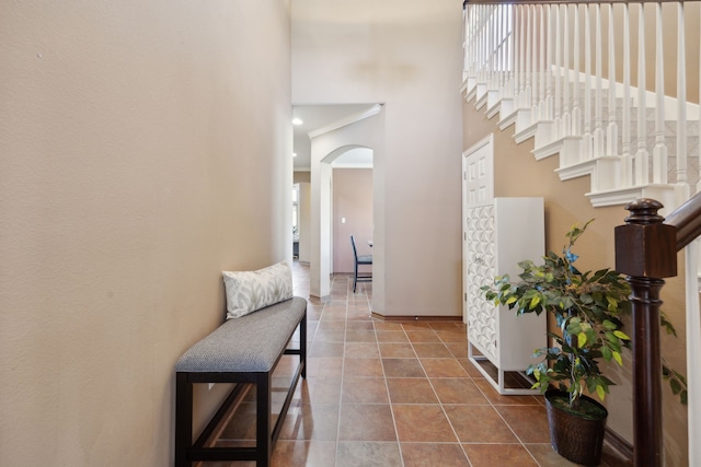 hall with arched walkways, a towering ceiling, baseboards, stairs, and tile patterned floors