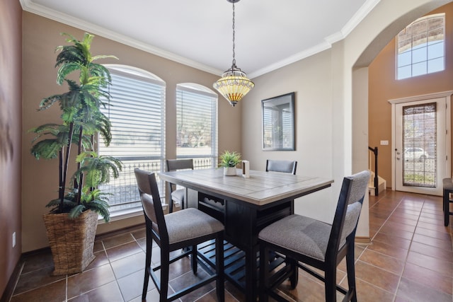 dining space with ornamental molding, arched walkways, and dark tile patterned flooring