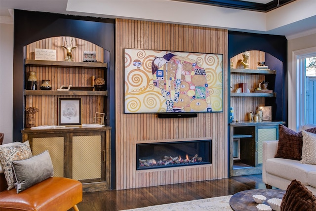 living room with a glass covered fireplace, wood finished floors, built in features, and crown molding