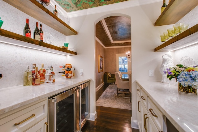 bar featuring arched walkways, beverage cooler, a bar, dark wood finished floors, and crown molding