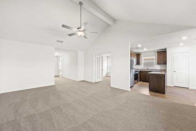 unfurnished living room with baseboards, light colored carpet, ceiling fan, beam ceiling, and a sink