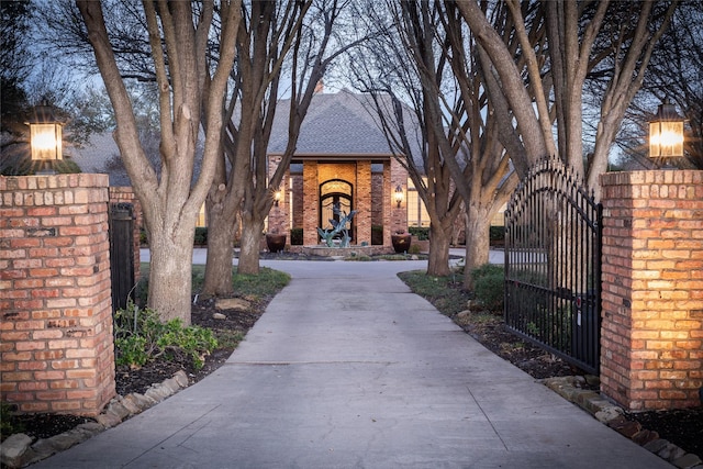 exterior space with a gate, brick siding, and roof with shingles