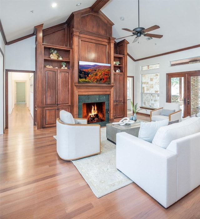 living room with crown molding, ceiling fan, light wood-style flooring, a fireplace, and high vaulted ceiling