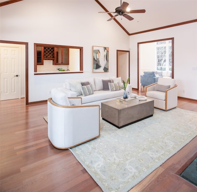 living room featuring high vaulted ceiling, ornamental molding, wood finished floors, baseboards, and ceiling fan