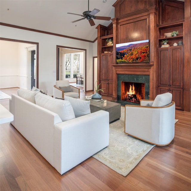 living room with a high end fireplace, ceiling fan, ornamental molding, vaulted ceiling, and light wood-style floors