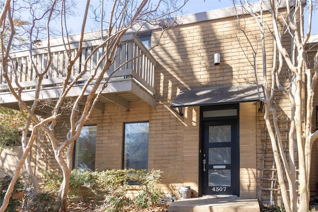 exterior space featuring brick siding, a shingled roof, and a balcony