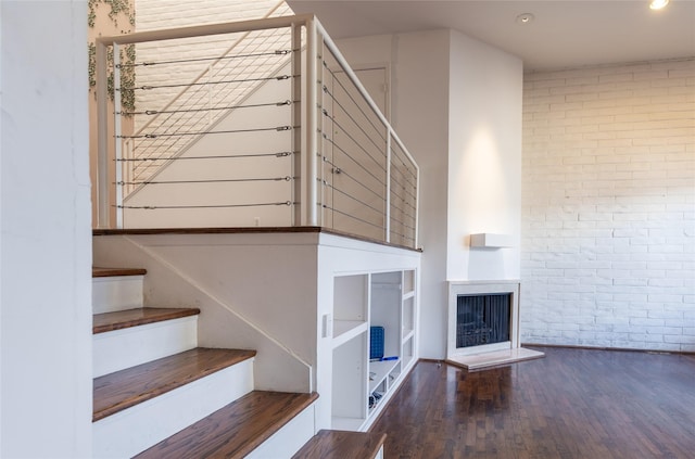 stairway with recessed lighting, a fireplace with raised hearth, brick wall, and wood finished floors