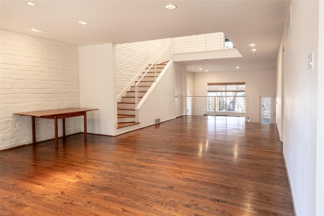 unfurnished room featuring recessed lighting, stairway, brick wall, and wood finished floors