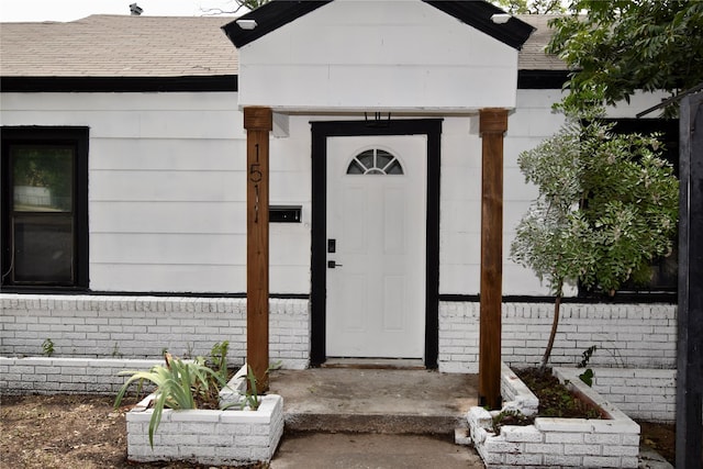 view of exterior entry with a shingled roof and brick siding