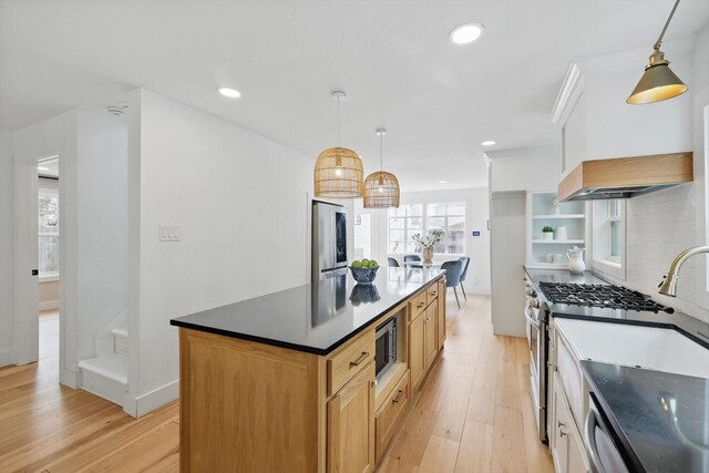 kitchen featuring custom exhaust hood, appliances with stainless steel finishes, dark countertops, light wood-type flooring, and backsplash