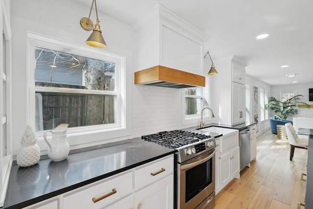 kitchen with dark countertops, light wood finished floors, decorative backsplash, appliances with stainless steel finishes, and white cabinets