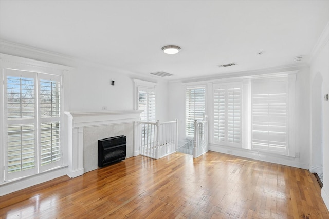 unfurnished living room featuring visible vents, wood-type flooring, a premium fireplace, and ornamental molding