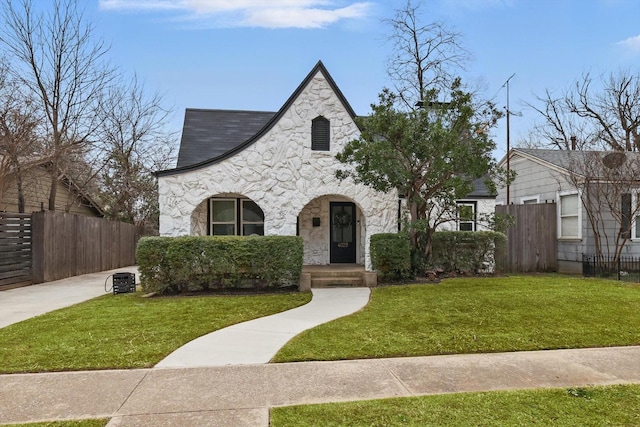 view of front facade featuring stone siding, a front lawn, and fence