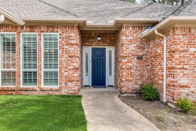 entrance to property featuring a shingled roof and brick siding