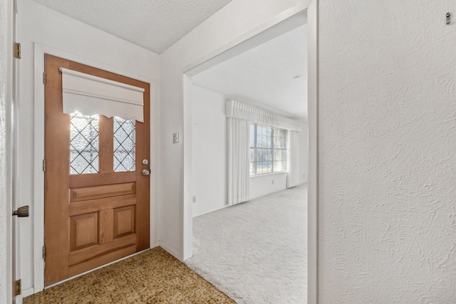 foyer entrance featuring carpet, a textured ceiling, and a textured wall