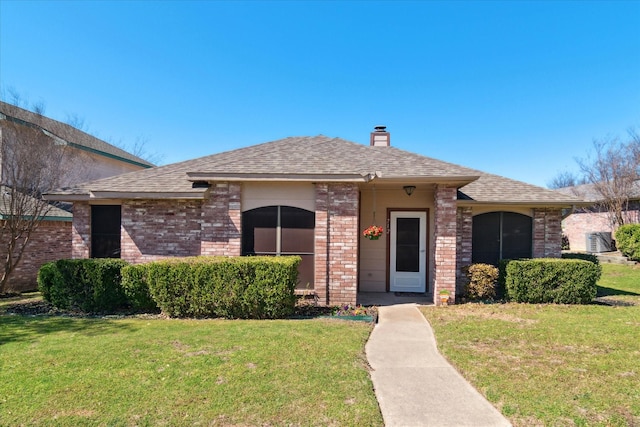 view of front facade with a shingled roof, a front yard, and brick siding