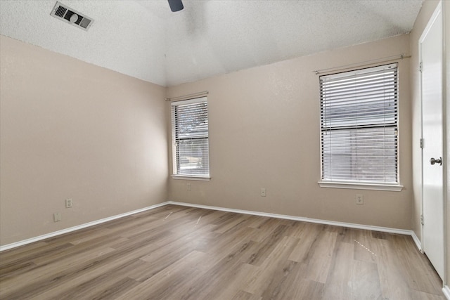 unfurnished room with a textured ceiling, lofted ceiling, visible vents, a ceiling fan, and light wood finished floors