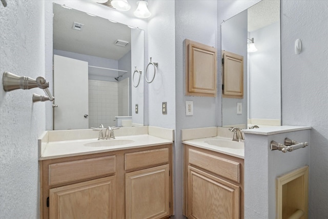 bathroom featuring a textured wall, two vanities, a sink, and walk in shower