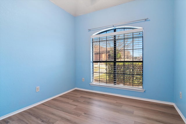 spare room with baseboards and wood finished floors