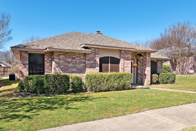 view of front facade with brick siding, central AC unit, a shingled roof, and a front yard