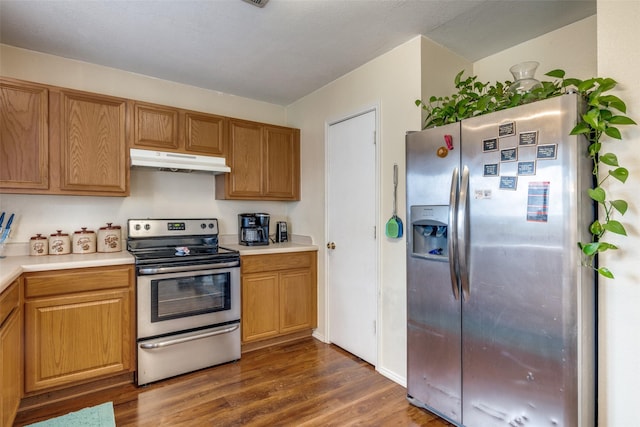 kitchen with appliances with stainless steel finishes, light countertops, under cabinet range hood, and dark wood-type flooring