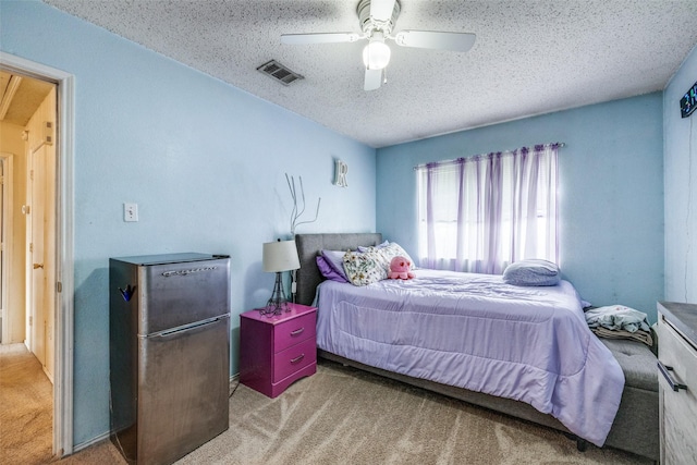 carpeted bedroom featuring a ceiling fan, freestanding refrigerator, visible vents, and a textured ceiling