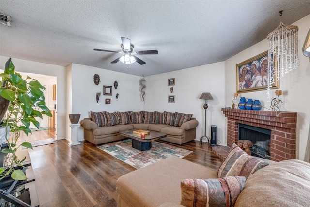 living room with a textured ceiling, a fireplace, a ceiling fan, and wood finished floors