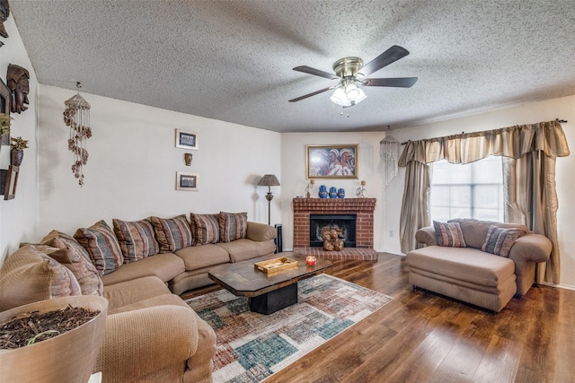 living room featuring a textured ceiling, a brick fireplace, wood finished floors, and a ceiling fan