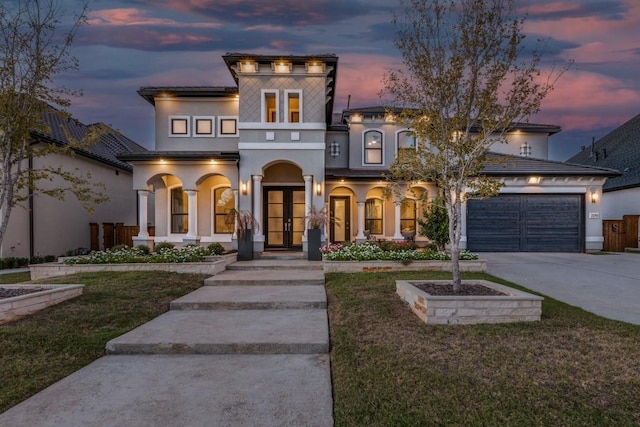 view of front of home with french doors, stucco siding, concrete driveway, a lawn, and a garage