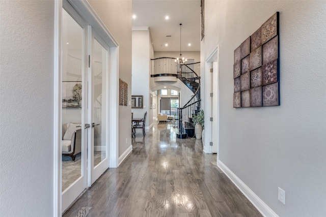 hall featuring baseboards, wood finished floors, an inviting chandelier, stairs, and french doors