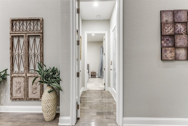 hallway with baseboards, wood finished floors, and a textured wall