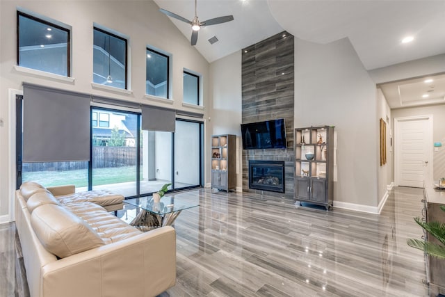 living area with visible vents, baseboards, a tile fireplace, ceiling fan, and high vaulted ceiling