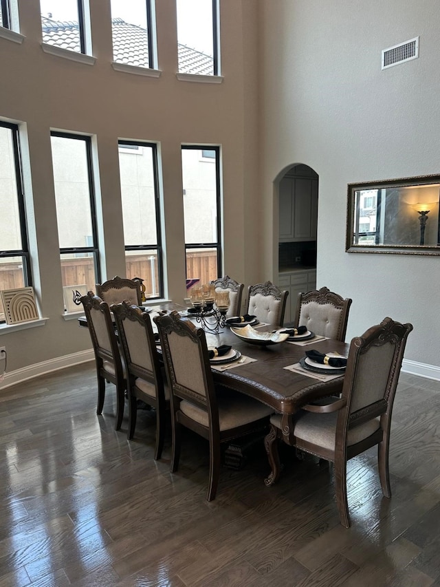 dining area with a towering ceiling, baseboards, visible vents, and dark wood-type flooring