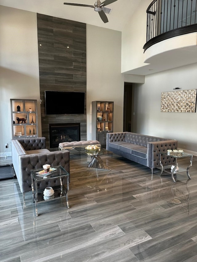 living room featuring a ceiling fan, a large fireplace, and a towering ceiling