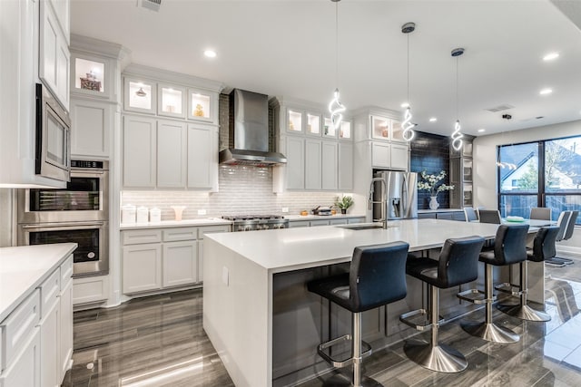 kitchen with a center island with sink, decorative backsplash, wall chimney exhaust hood, stainless steel appliances, and light countertops