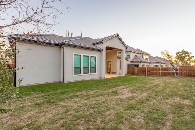 rear view of property featuring a yard, fence, a patio, and stucco siding