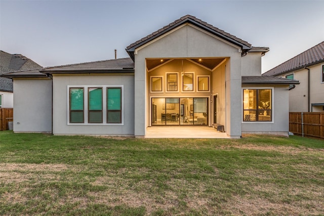 rear view of house with a yard, a patio area, fence, and stucco siding