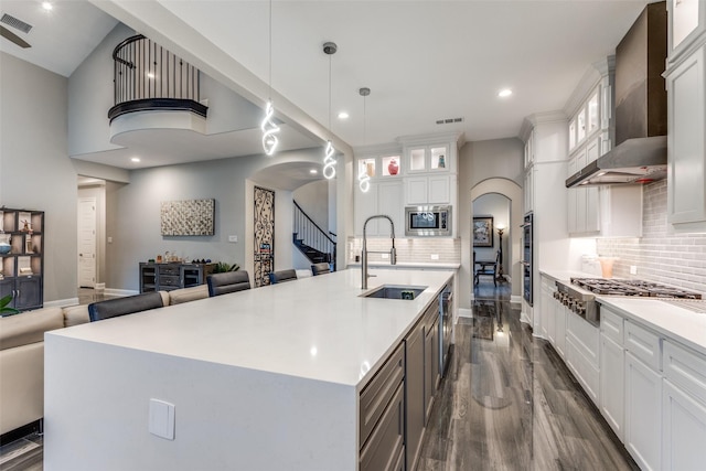 kitchen featuring arched walkways, appliances with stainless steel finishes, open floor plan, a sink, and wall chimney range hood