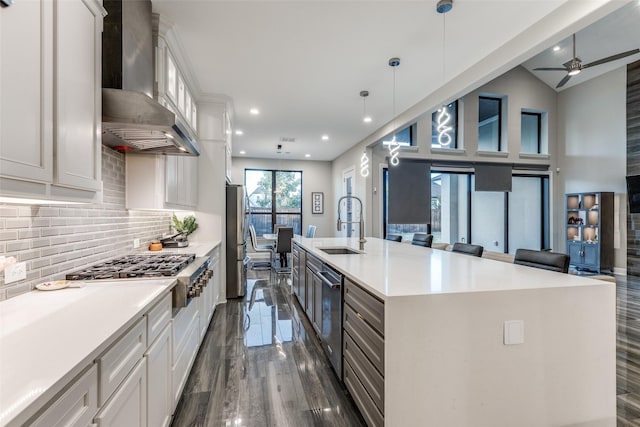 kitchen featuring appliances with stainless steel finishes, open floor plan, a sink, and wall chimney range hood