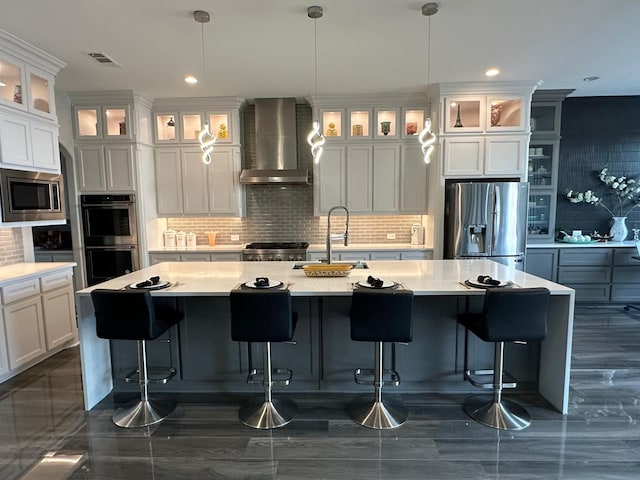 kitchen featuring visible vents, wall chimney exhaust hood, appliances with stainless steel finishes, a sink, and backsplash