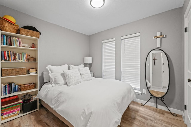 bedroom featuring multiple windows, baseboards, and wood finished floors