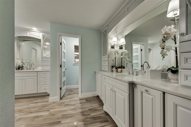 bathroom featuring wood finished floors, baseboards, recessed lighting, two vanities, and a sink