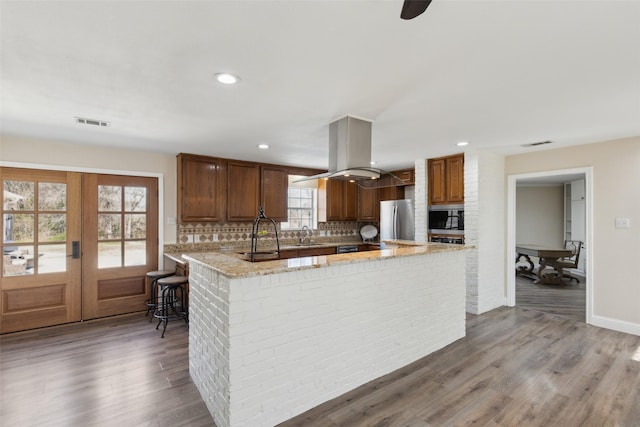 kitchen with light stone countertops, stainless steel appliances, a peninsula, decorative backsplash, and visible vents