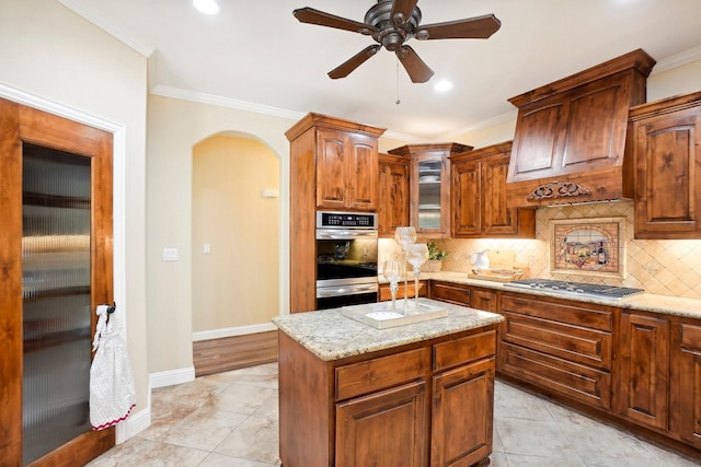 kitchen with light stone counters, arched walkways, tasteful backsplash, appliances with stainless steel finishes, and ornamental molding