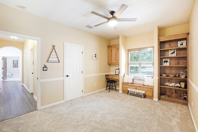 unfurnished office featuring carpet, visible vents, arched walkways, and ceiling fan