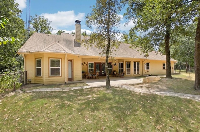 rear view of house featuring a chimney, fence, a lawn, and a patio