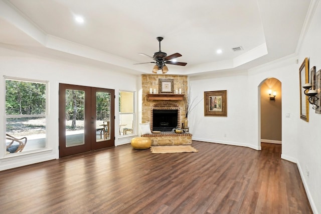 unfurnished living room with dark wood-style floors, arched walkways, a raised ceiling, and a large fireplace