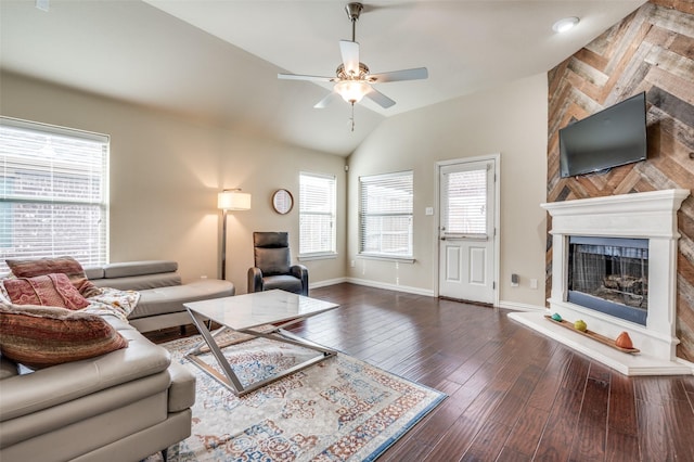 living room with hardwood / wood-style floors, a ceiling fan, baseboards, a fireplace with raised hearth, and vaulted ceiling