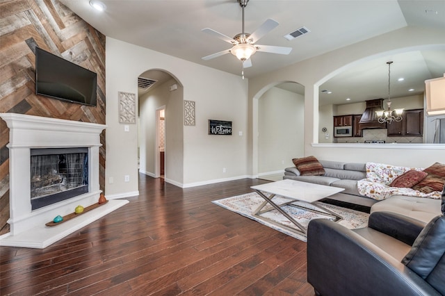 living area with visible vents, ceiling fan with notable chandelier, a large fireplace, and dark wood-type flooring