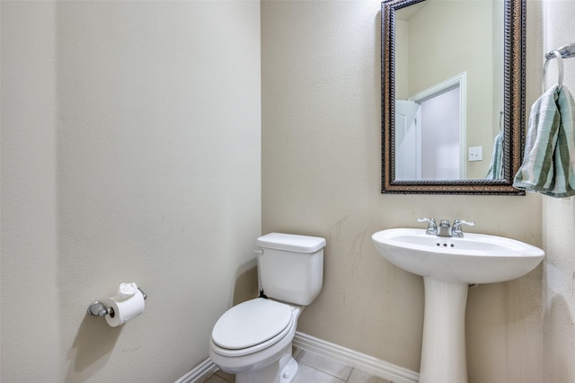 half bath with tile patterned floors, baseboards, toilet, and a sink